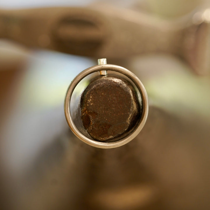 Le rivet d'argent, matté à la main dans le titane — le petit point clair qui la signe.